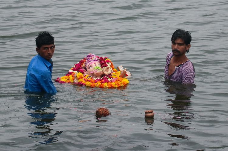 Men waist deep in water carry a statue adorned with flowers into the lake of the Jal Mahal palace.